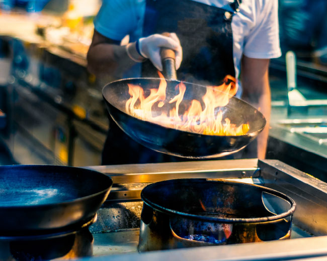 Đầu bếp dùng chảo wok trong bếp với lửa bùng trong chảo